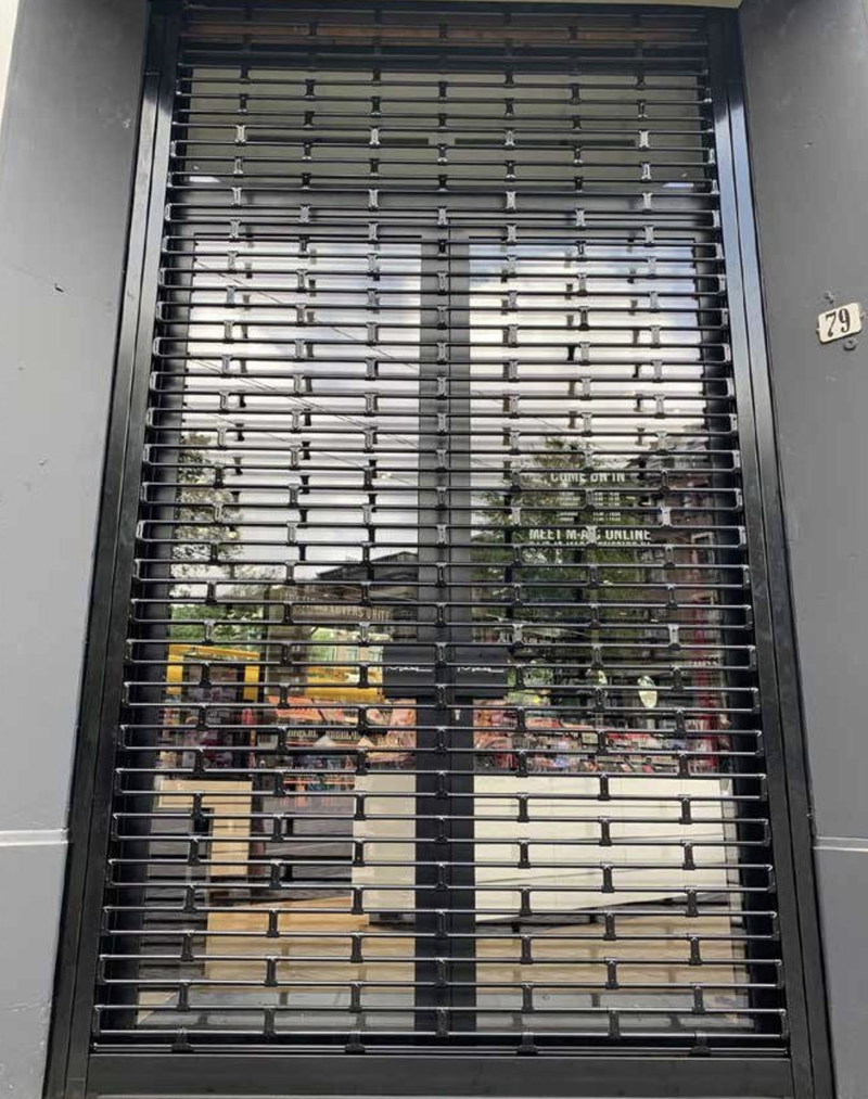 Black perforated rolling security gate on a storefront, showing reflections and interior items.