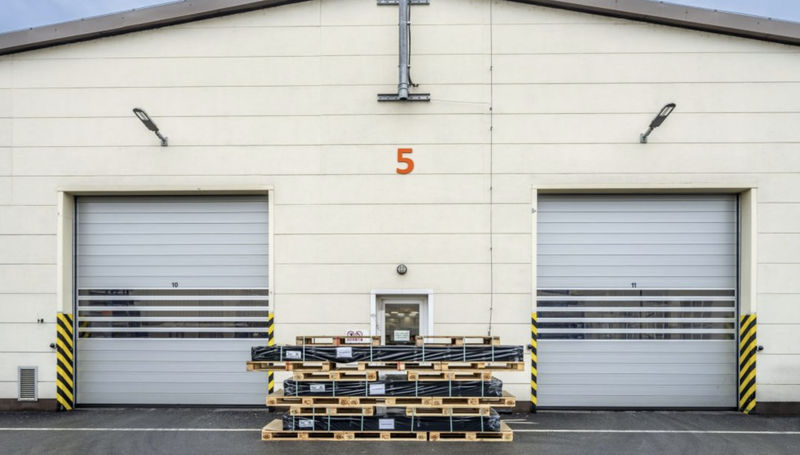 Logistics warehouse exterior with two loading dock doors, number 5 above, and stacked pallets of goods.