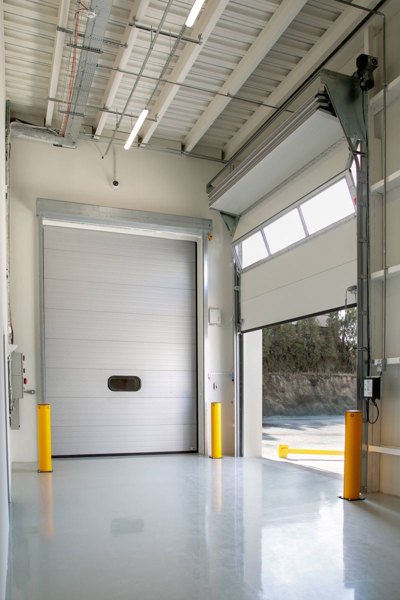 Modern warehouse interior with two industrial sectional doors, one closed and one partially open, showing the loading dock.